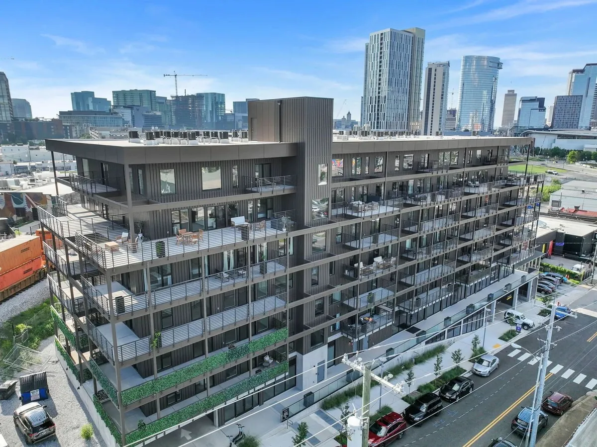 A striking exterior shot of the modern building with balconies and a rooftop terrace, set against the Nashville city skyline. The image conveys urban connectivity and proximity to city attractions and business districts.