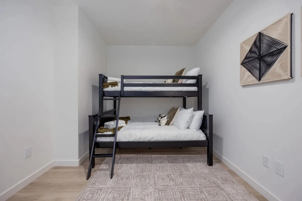 A playful bedroom setup with a sturdy bunk bed, colorful decorative wall art, and a soft area rug. The space is designed for both sleep and fun, supporting family gatherings and group stays, with plenty of room for children or friends.
