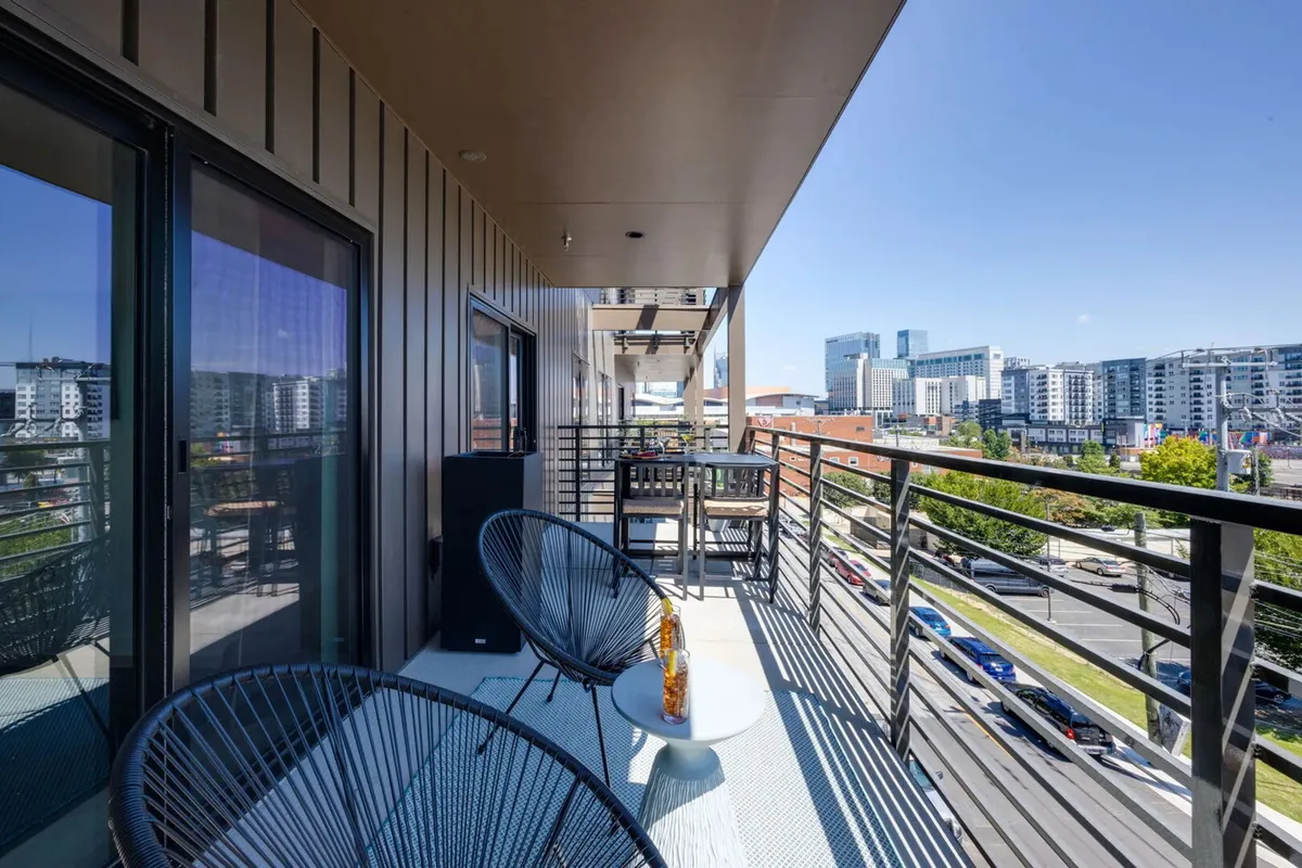 A private balcony with comfortable seating and a small table overlooking the Nashville city skyline. The tranquil urban backdrop is visible, suggesting a spot for unwinding or socializing after a busy day.