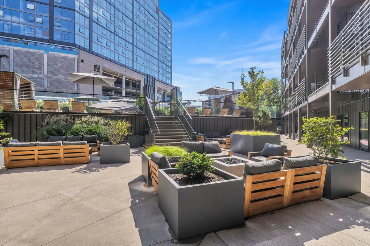 A rooftop deck featuring comfortable lounge seating, contemporary landscaping, and a stylish staircase leading to elevated social spaces. The area is inviting for both daytime relaxation and evening gatherings, with the modern building facade in the background.