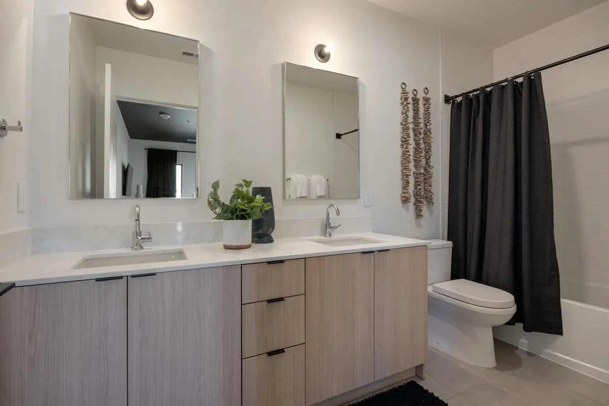 A modern bathroom featuring a double vanity sink, expansive mirrors, and textured wall decor. The room is bright and inviting, evoking the feel of a spa with space for personal grooming and relaxation.