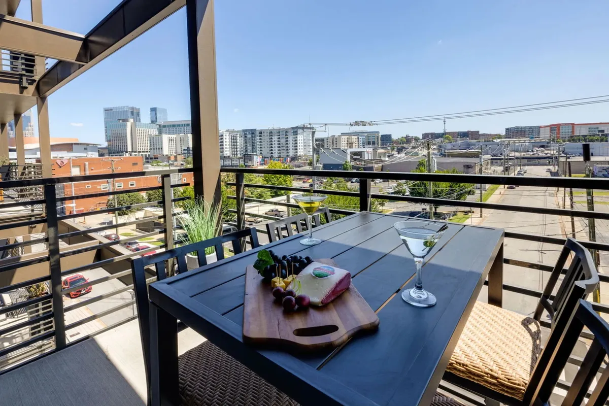 An elegant balcony dining setup with a charcuterie board and cocktail on the table, overlooking the city skyline at sunset. The warm glow of evening light creates an inviting ambiance for al fresco gatherings.