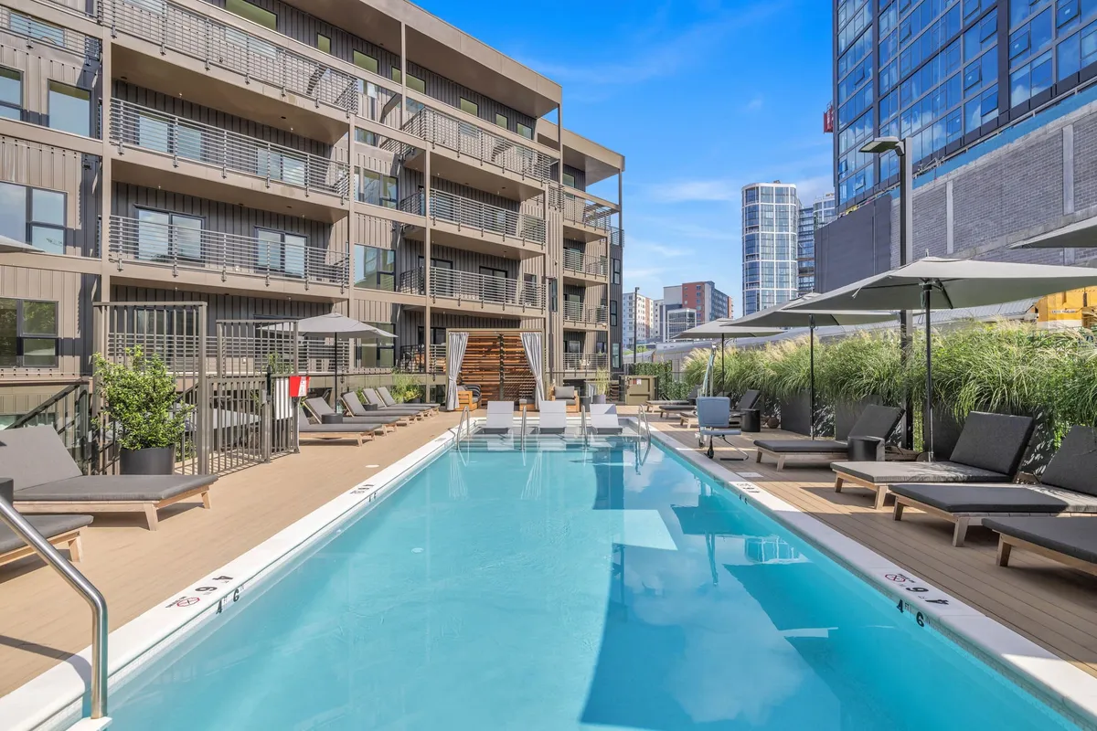 An inviting exterior view of a modern swimming pool surrounded by lounge chairs and the building facade. The pool area looks relaxing, perfect for both energetic play and unwinding after a day out.