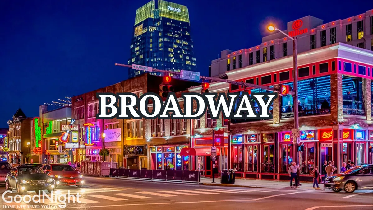 A lively exterior street scene on Broadway featuring colorful neon signs, bustling crowds, cars, and buildings. The image radiates the nightlife and vibrancy that Nashville is famous for, with people heading to live music venues, restaurants, and shops.