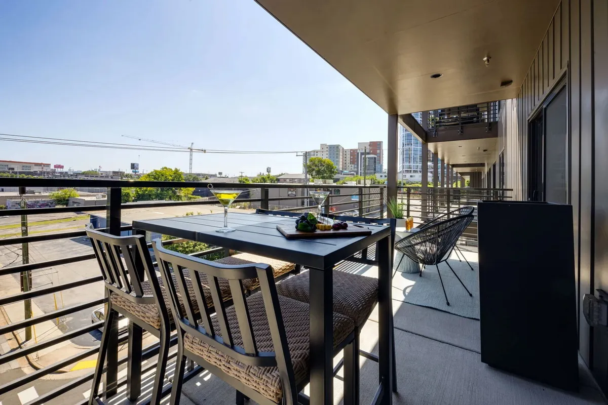 A stylish private balcony outfitted with comfortable seating and a modern outdoor dining table, set against a sweeping view of the Nashville skyline. The setting suggests a place for enjoying meals, sipping cocktails, or gathering with friends as the sun sets.